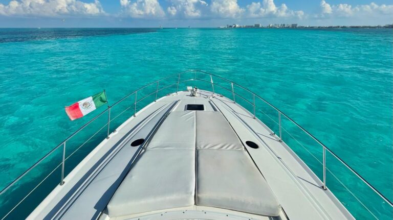 Side view of 60 ft Sea Ray Triton luxury yacht charter anchored in turquoise Caribbean water with Mexico flag flying and dramatic cloud sky