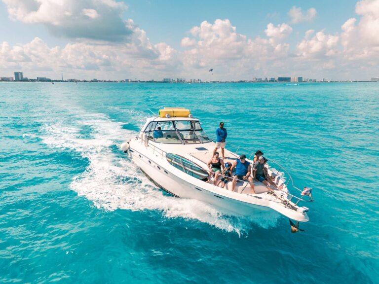 Aerial drone view of 46 ft Sea Ray Sundancer Caiman yacht charter at speed in turquoise Caribbean water near Cancun, guests gathered on deck enjoying luxury boat rental