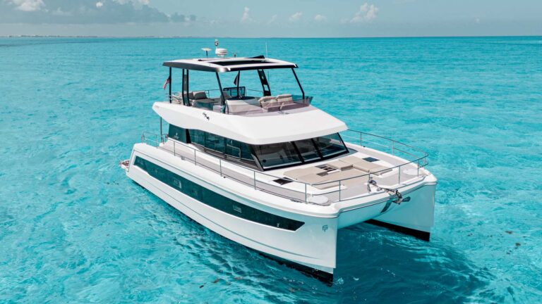 Stern quarter view of 51 ft Fountain Pajot Libert� MY44 power catamaran with open teak swim platform and name plate, anchored in turquoise Caribbean