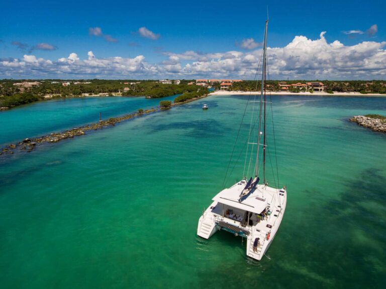 Bird's-eye aerial view of 42 ft Lagoon catamaran sailing yacht anchored in crystal-clear turquoise Caribbean waters with guests swimming alongside the catamaran on inflatable floats