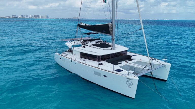 Aerial starboard view of 45 ft Lagoon Beluga catamaran anchored in turquoise Caribbean waters off Cancun, full hull, mast and white trampoline visible, luxury charter