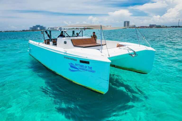 45 ft Rhythms of the Caribbean Sunset motor catamaran group charter anchored in turquoise water near Cancun, bright turquoise hull with crew at helm and hotel zone skyline behind