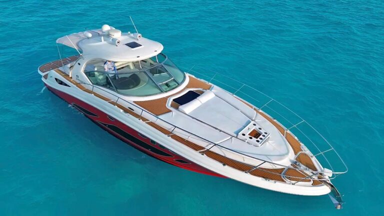 Side profile of the bold red and white 45 ft Sea Ray Red Fire luxury sport boat rental cruising in turquoise Caribbean waters with the Cancun hotel zone coastline in the background