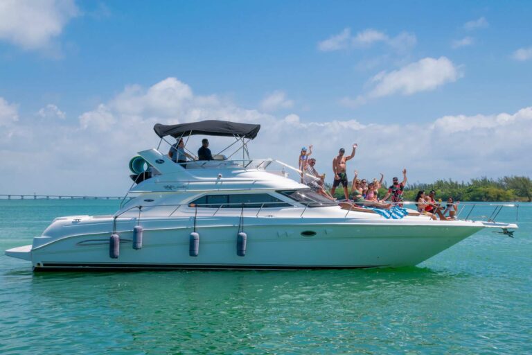 Side view of 48 ft Sea Ray Flybridge Venezia luxury yacht charter with group of guests celebrating on foredeck, anchored near Isla Mujeres causeway in Cancun