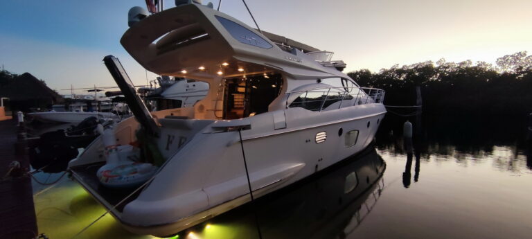 Rear view of the 50 ft Azimut yacht for groups cruising through Cancun mangrove lagoon, guests on flybridge, swim platform and stern deck clearly visible under bright blue skies