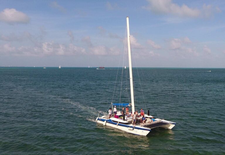 Aerial side view of 30 ft Eagle sailing catamaran underway with guests on deck and sailboats on the horizon during a Cancun yacht charter