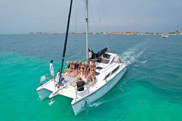 Aerial view of 35 ft Gemini catamaran Talisman cruising turquoise Isla Mujeres waters with guests in straw hats relaxing on the front deck