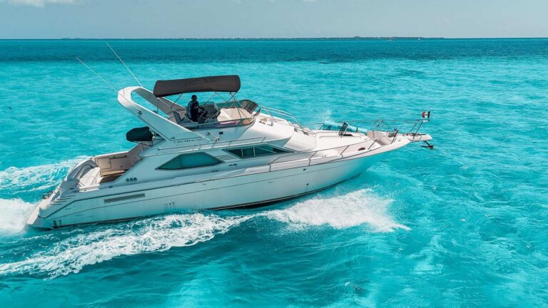 Side aerial view of 47 ft Sea Ray flybridge Bella Donna anchored in turquoise Caribbean water near Cancun with Mexican flag on the luxury yacht charter.