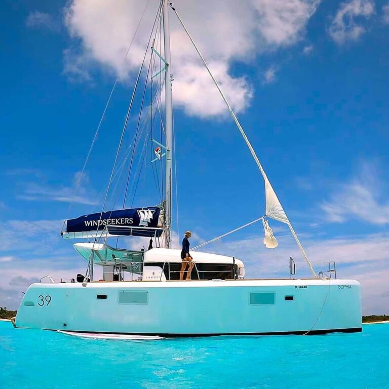 Lagoon 39 catamaran Sophia Windseekers anchored in brilliant turquoise Caribbean water at Cozumel, tall mast and mainsail cover, crew member on deck.