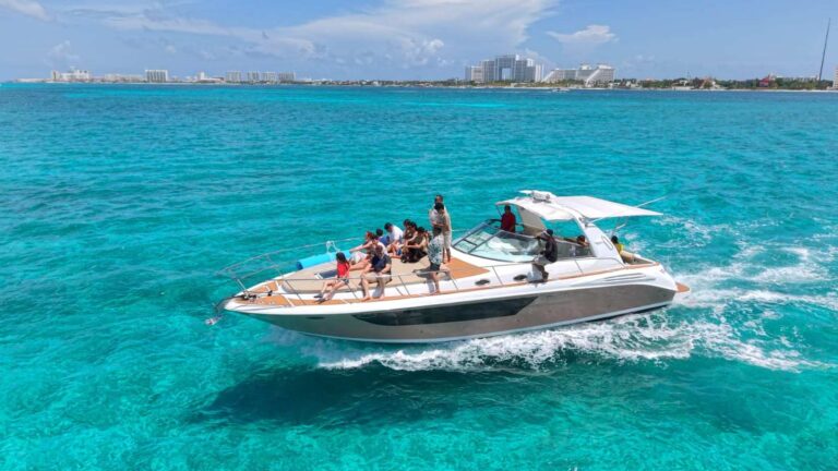 Group of fifteen guests aboard 42 ft Sea Ray Dorado Sensus charter at speed on turquoise Caribbean with Cancun Hotel Zone skyline behind.