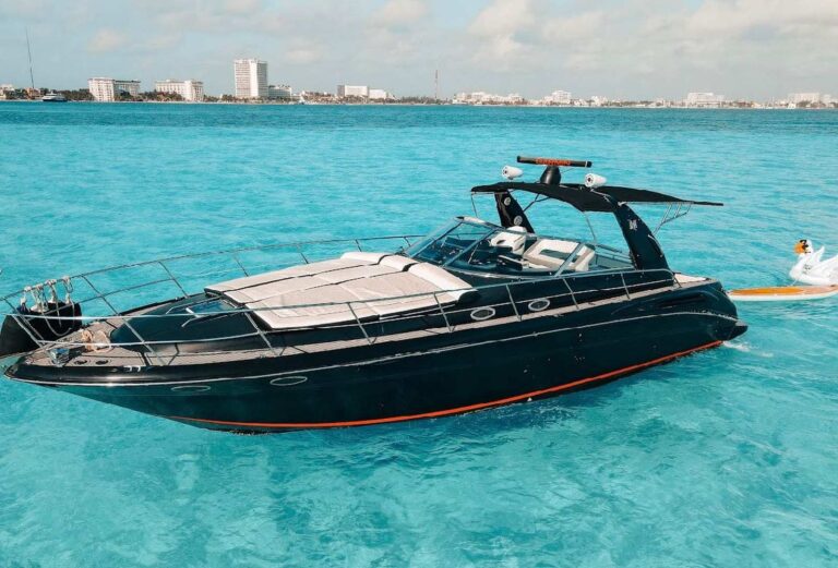 Black 43 ft Sea Ray luxury yacht charter anchored in turquoise Caribbean water with Cancun Hotel Zone skyline in background, swan float alongside.