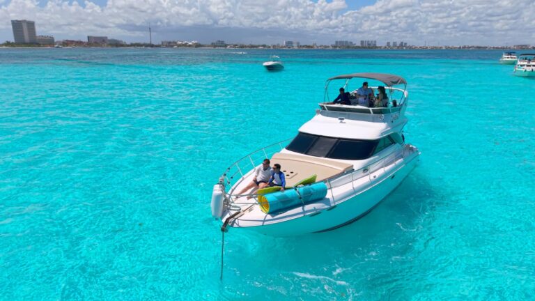 Aerial view of 44 ft Sea Ray flybridge yacht charter anchored in crystal-clear turquoise Caribbean water near Cancun, guests on bow and upper deck.
