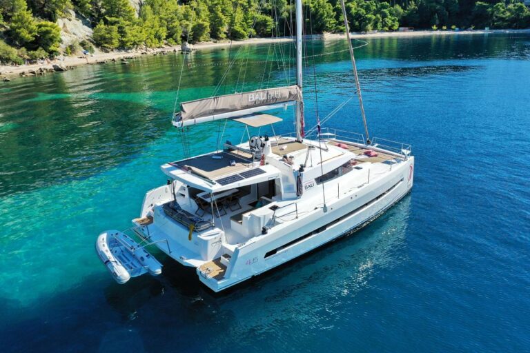 Aerial view of 45 ft Bali 4.5 catamaran rental anchored in turquoise forested cove with dinghy on stern, solar panels and mast visible, Cancun.