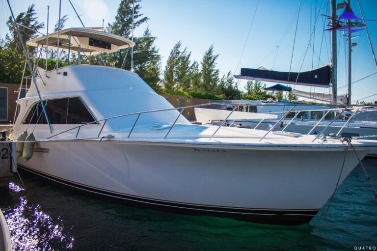 Side profile of 48 ft Post Kalifa sportfishing boat docked at Cancun marina with tall outriggers, enclosed flybridge, white hull and blue accent stripe.