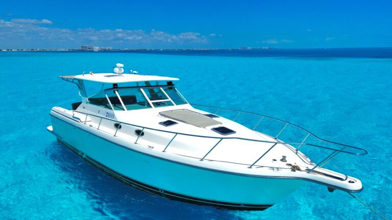 Side profile of 48 ft Tiara luxury yacht rental anchored in brilliant turquoise Caribbean near Cancun, bow sun pad and hardtop flybridge canopy visible.