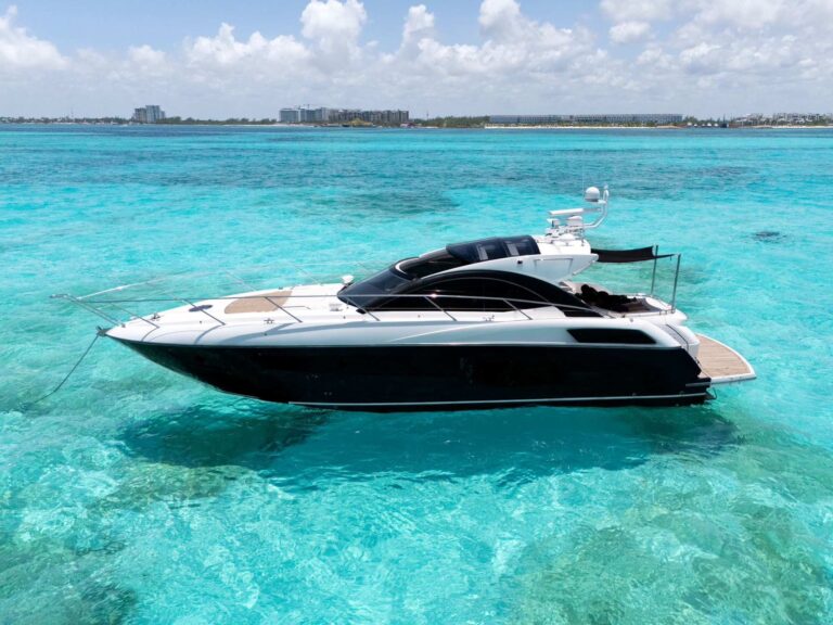 54 ft Sunseeker San Remo Black luxury yacht charter anchored in crystal-clear turquoise Caribbean water near Cancun with resort skyline in background.