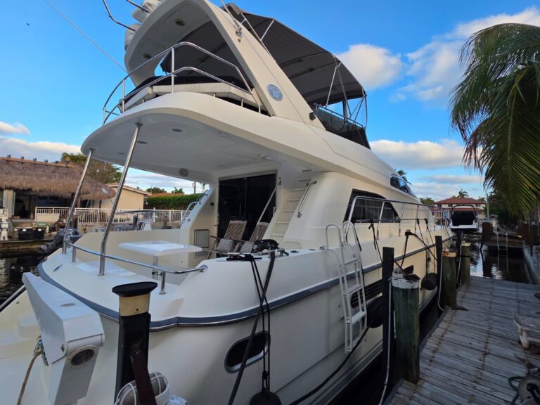 65 ft Neptunus luxury flybridge motor yacht docked at canal marina, teak aft deck with captain chairs, palm trees and thatched buildings alongside.